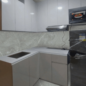 Custom modular kitchen cabinet with glossy white finish, marble backsplash, and modern L-shaped layout.